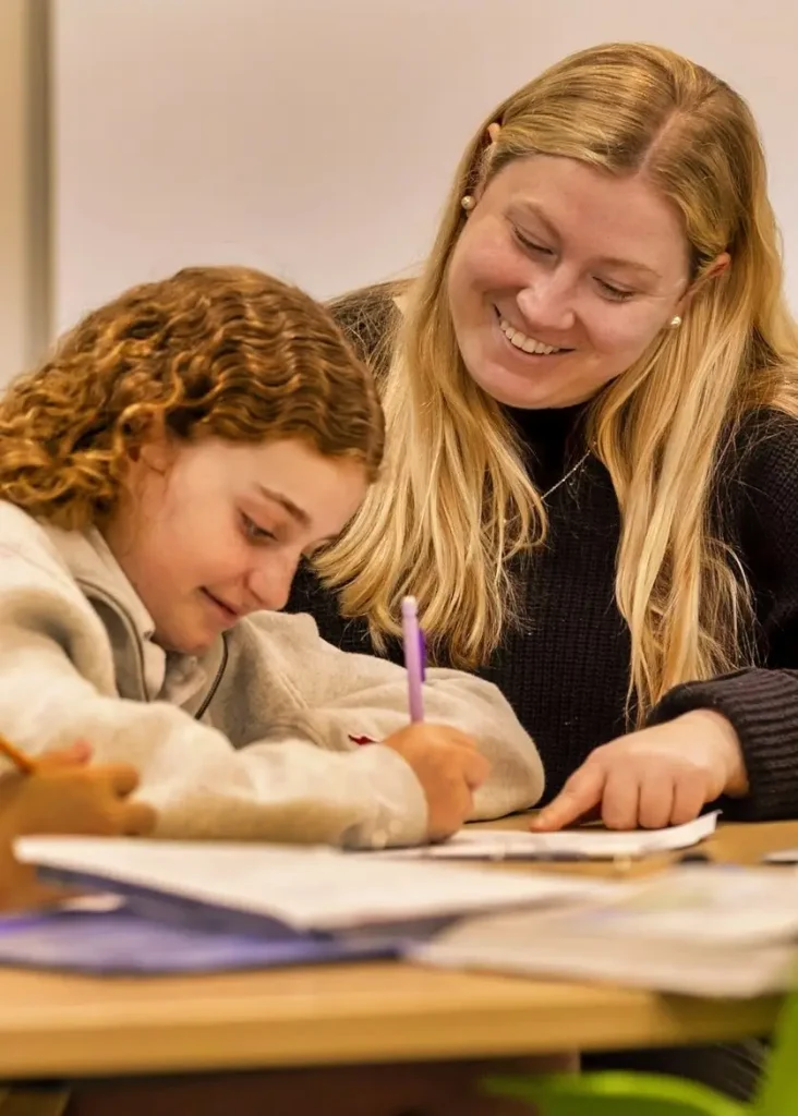 Holy Child teacher smiling while helping a young student with classwork